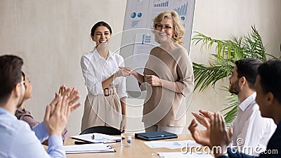 Smiling 60s leader shaking hands with happy young arabic colleague. Stock Photo