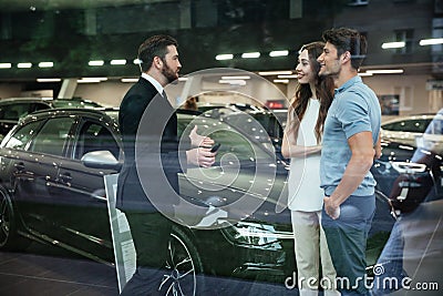 Smiling salesman showing new car to a couple in showroom Stock Photo