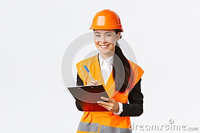 Smiling satisfied asian female construction engineer leading inspection at enterprise, wearing safety helmet and Stock Photo