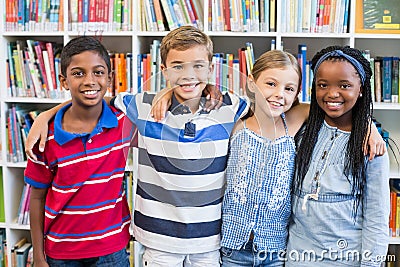 Smiling school kids standing with arm around in library Stock Photo