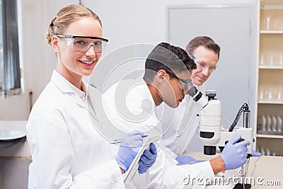 Smiling scientist looking at camera while colleagues working with microscope Stock Photo