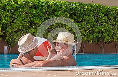 Smiling senior couple plays in the pool with an inflatable ball. Happy retirees enjoy summer holidays under the sun Stock Photo