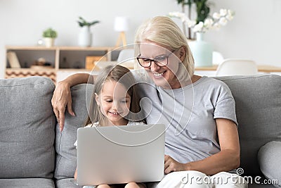 Smiling grandma and cute kid granddaughter watching cartoons on Stock Photo