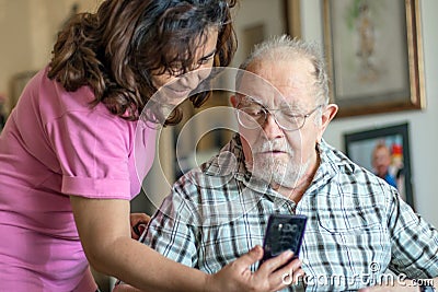 A Smiling senior man and caregiver with smartphone are doing a videocall Stock Photo