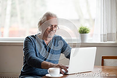 Smiling senior man in glasses working on laptop at home Stock Photo