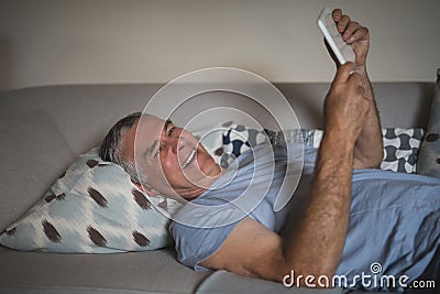 Smiling senior man holding digital tablet while lying on sofa at home Stock Photo