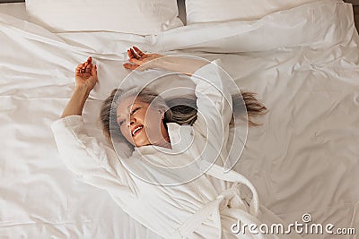 Smiling senior woman in a bathrobe lying on a bed and looking away. Female relaxing in a hotel room Stock Photo