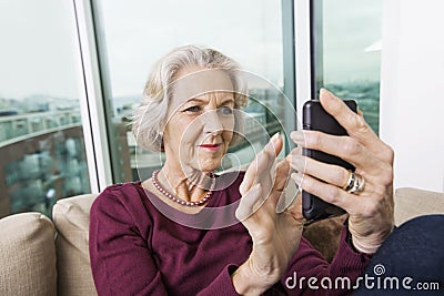 Smiling senior woman text messaging on smart phone at home Stock Photo