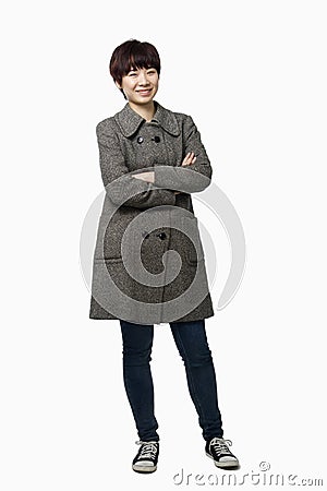 Smiling short haired young woman with arms crossed in a grey coat, studio shot, portrait Stock Photo