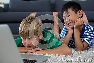 Smiling siblings lying on rug and using laptop in living room Stock Photo