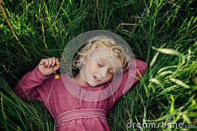 Beautiful Caucasian girl in tall grass on meadow at sunset.Smiling sleeping dreaming Caucasian girl with closed eyes in grass Stock Photo