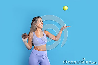 Smiling slim young caucasian woman in sportswear with donut in hand throws up green apple, has fun Stock Photo