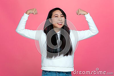 Smiling strong independent asian young girl showing muscles gesture on pink studio background. Achievements concept Stock Photo