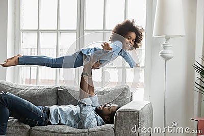 Young african ethnicity daddy lifting on hands happy daughter. Stock Photo
