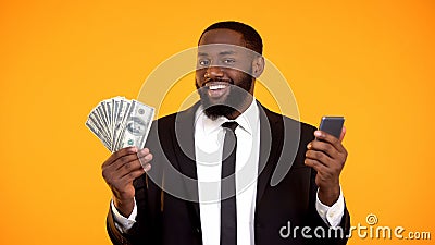 Smiling Successful black male in suit holding phone and dollar bills, cashback Stock Photo