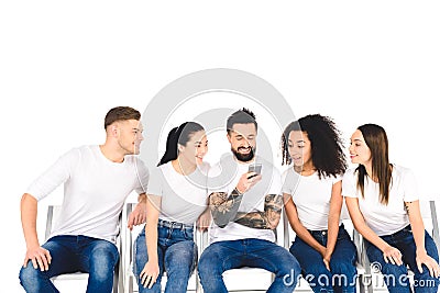 smiling tattooed man using smartphone while multiethnic curious young people looking at screen isolated Stock Photo