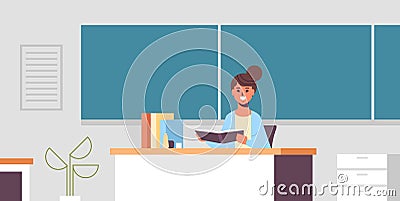 Smiling teacher sitting at desk woman checking students copybook in front of green chalk board education concept modern Vector Illustration