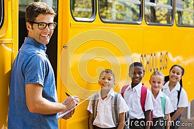 Smiling teacher updating check list of kids while entering in bus Stock Photo