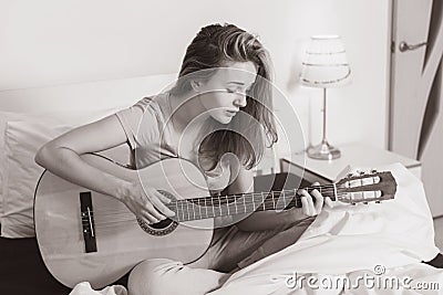 Smiling teen girl playing on guitar on the bed at home Stock Photo