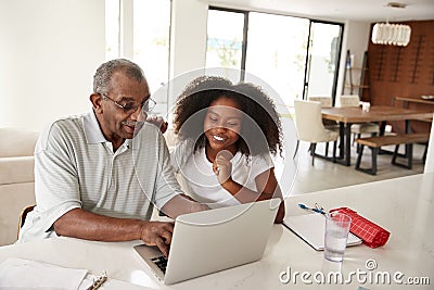 Smiling teenage African American girl sitting at home helping her grandfather use a laptop computer Stock Photo