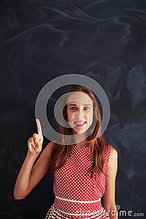 Smiling teenage girl in front of blackboard pointing upwards wit Stock Photo