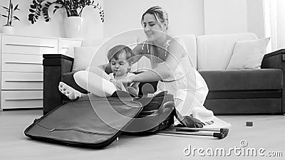 Cute smiling toddler boy sitting in suitcase while mother packing things for traveling Stock Photo