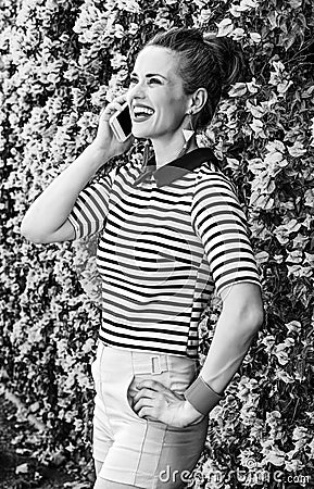 Smiling trendy woman near flowers bed speaking on cell phone Stock Photo