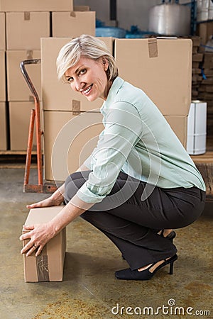 Smiling warehouse manager picking up cardboard box Stock Photo