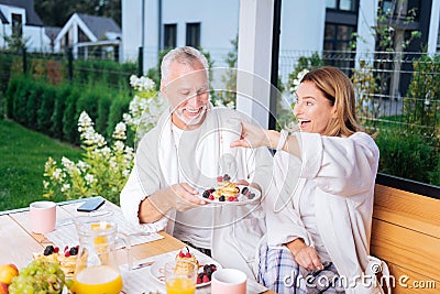 Smiling wife putting some sweet honey on pancakes of her beaming husband Stock Photo