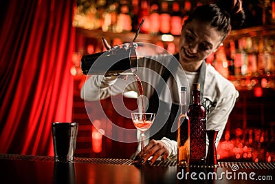 smiling woman bartender gently pours cocktail from shaker into glass at bar counter Stock Photo