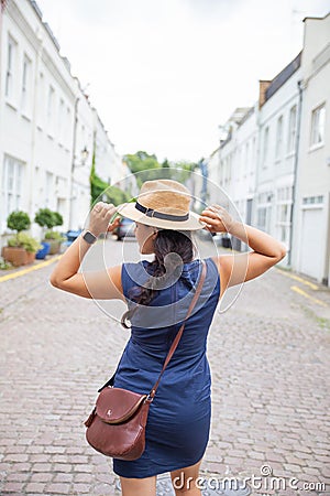 Smiling Woman in Blue Dress From Behind, Calmly Adjusts Her Hat with Both Hands Stock Photo