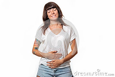 A smiling woman closed her eyes and holds her stomach with hands. White background. Copy space. Concept of good digestion and Stock Photo