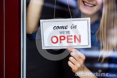 Smiling woman hanging open sign on small local business shop door window Stock Photo