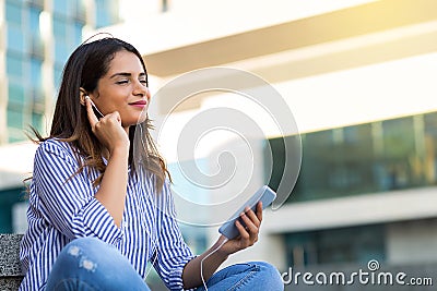 Smiling woman listening to music in headphones, enjoying sunny weather outdoors Stock Photo