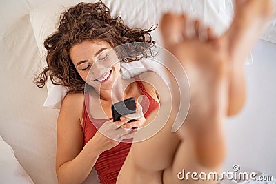 Happy girl using phone while lying on bed in the morning Stock Photo