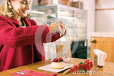 Smiling mature woman with facial wrinkles putting sugar in her coffee Stock Photo