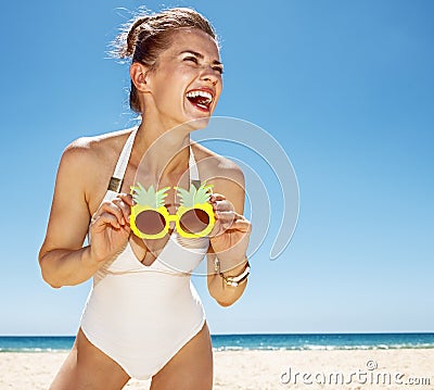 Smiling woman at sandy beach holding funky pineapple glasses Stock Photo