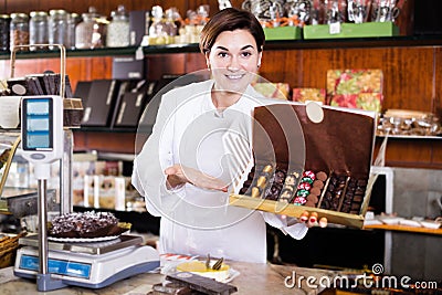 Smiling woman seller showing box of chocolate sweets Stock Photo