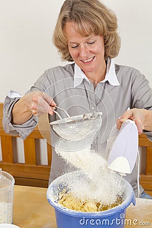 Smiling woman sieving flour into dough Stock Photo