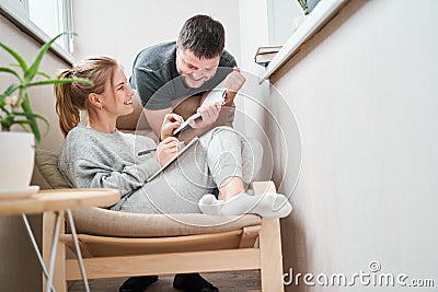 Smiling woman sitting on beige armchair and brunet standing beside her on balcony in apartment Stock Photo