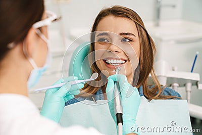 Smiling woman sitting in medical chair while dentist fixing her teeth Stock Photo
