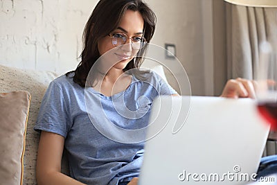 Smiling woman sitting on sofa with laptop computer and chating with friends Stock Photo