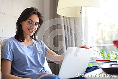 Smiling woman sitting on sofa with laptop computer and chating with friends Stock Photo