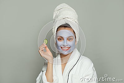 Smiling woman spa model in moisturizing cosmetic face mask with cucumber on white background. Female in white bathrobe and towel. Stock Photo