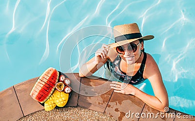 Smiling woman in straw hat in sunglasses swimming in pool and enjoying fresh tropical fruits Stock Photo