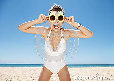 Smiling woman in swimsuit and funky pineapple glasses at beach Stock Photo