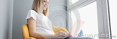 Smiling woman working on laptop while sitting in chair Stock Photo