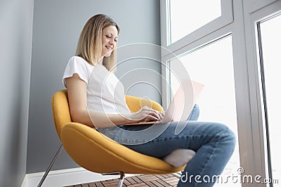 Smiling woman working on laptop while sitting in chair Stock Photo