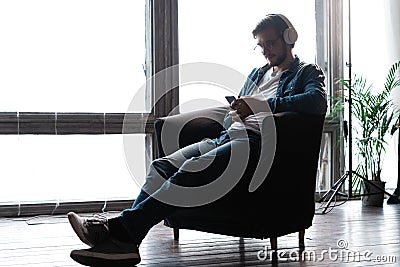 Smiling young adult man wearing wireless headphones listening mobile music on smartphone Stock Photo