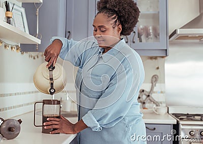 Smiling young African woman preparing fresh coffee in her kitchen Stock Photo